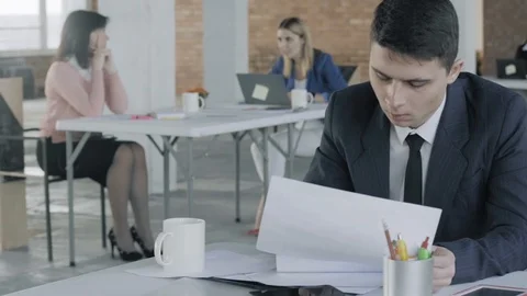 Employee man working at a table with documents in the office. Colleagues work in Stock Footage 124662357