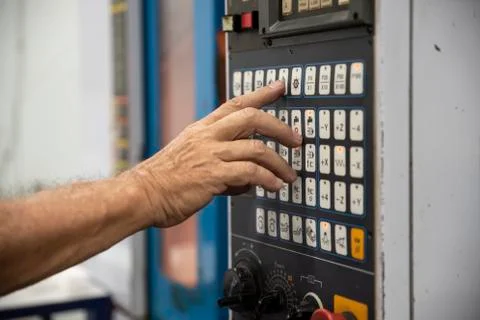 An employee presses the button on the control panel of CNC Stock Photos