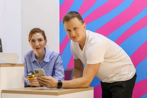 Employee smiling at customer while holding scanner and checking phone at counter Stock Photos