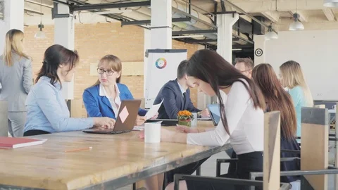 Employees hold a meeting at a large table in a creative office space. Work and Stock Footage 109367987
