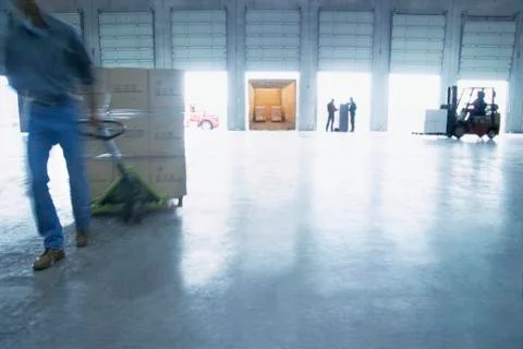 Employees pulling pallets and loading cardboard boxes of products into truck Stock Photos