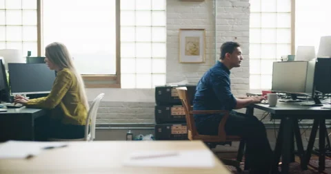 Employees sit and stand at computers and drink coffee in modern well lit design Stock Footage 199462089