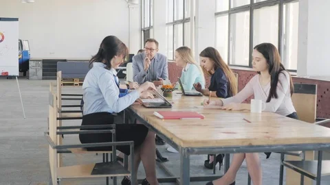 Employees sit at a large table and hold a meeting. A woman manager gets up and Stock Footage 109375438