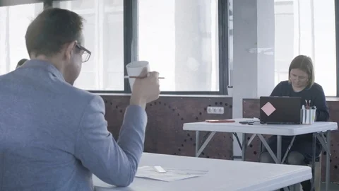 Employees work in the office. In the foreground, the manager is drinking tea. In Stock Footage 124705925