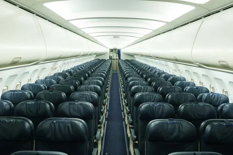 Empty airplane interior with rows of seats and dim lighting showing a quiet.. Stock Photos