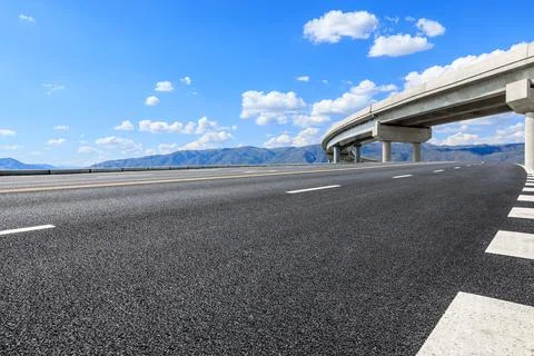 Empty asphalt road and bridge with mountain scenery under blue sky. Stock Photos