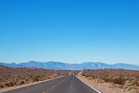 Empty asphalt road through the desert in a sunny day with mountains Stock Photos