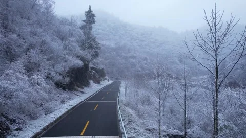 Empty asphalt road winding through snowy mountain forest in cold winter season Stock Footage 347046990