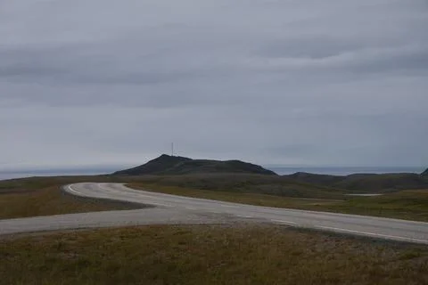 An empty asphalt road winding through arctic tundra towards coastal cliffs an Stock Photos