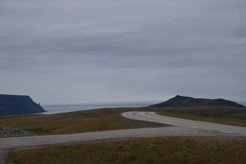 An empty asphalt road winding through arctic tundra towards coastal cliffs an Stock Photos