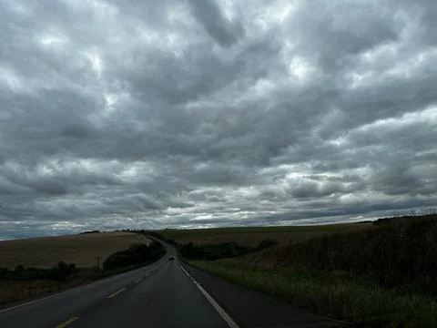 Empty asphalt road winding through rural landscape under dramatic cloudy sky Stock Photos