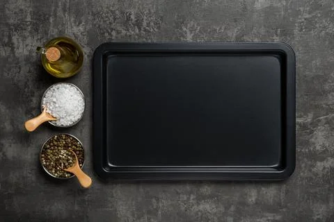Empty baking sheet, olive oil jar, salt and pepper over black background. Stock Photos