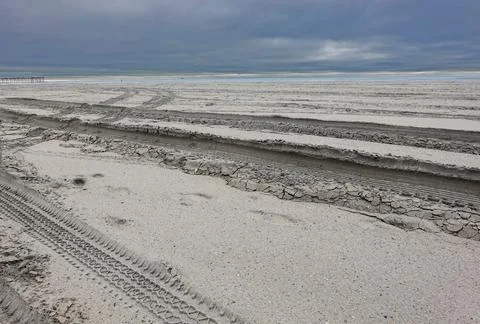 Empty barron secluded beach by the ocean with deep tire tracks in the sand Stock Photos