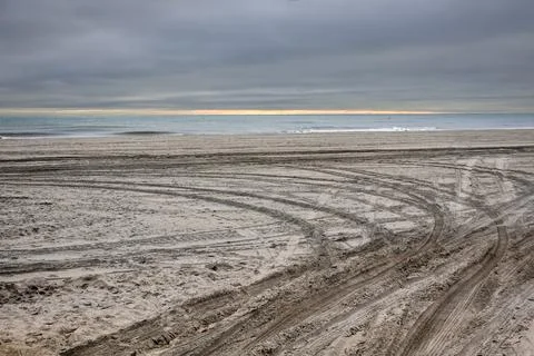 Empty barron secluded beach by the ocean with deep tire tracks in the sand Stock Photos