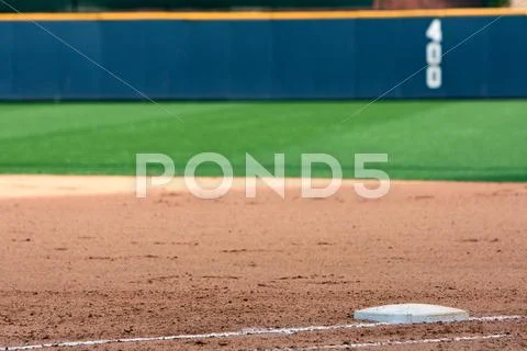 Empty baseball field highlights first base and outfield wall. Stock Photos