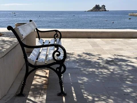 An empty beach bench in the resort opposite the sea bay and a small island Stock Photos