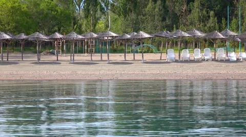 Empty beach, cane sun umbrellas and sunbeds against trees. 4K low season video Stock Footage 64026384