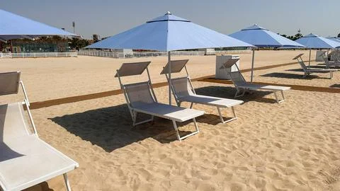 Empty beach chairs and umbrellas on sandy shore under clear blue sky in summer Stock Photos