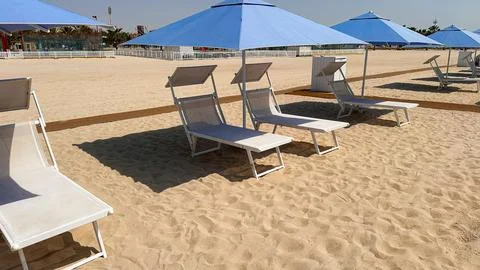 Empty beach chairs and umbrellas arranged on sandy shore under clear sky Stock Photos