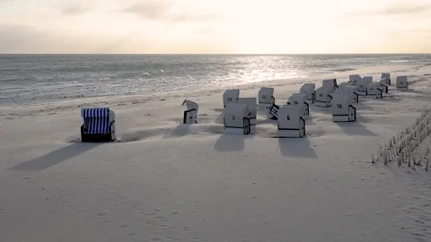 Empty beach chairs are bathed in the light of the rising sun on the beach at Stock Footage 334519403
