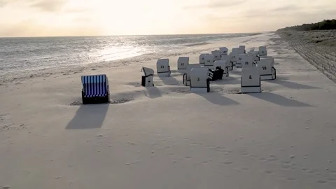Empty beach chairs are bathed in the light of the rising sun on the beach at Vídeos de archivo 334522016
