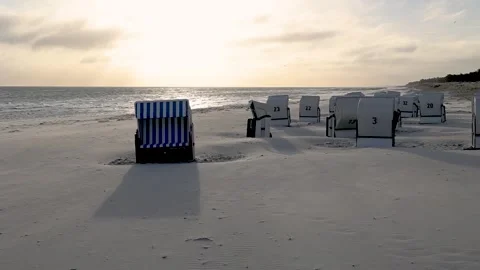 Empty beach chairs are bathed in the light of the rising sun on the beach at Stock Footage 334525260
