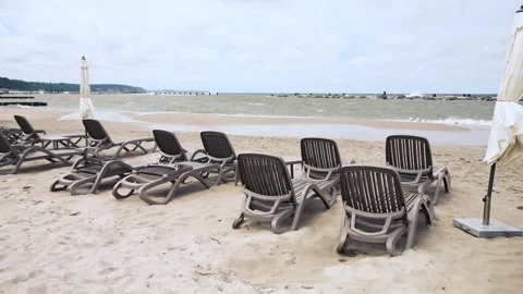 Empty beach loungers arranged on sandy shore under cloudy sky by calm sea Stock Footage 337479326