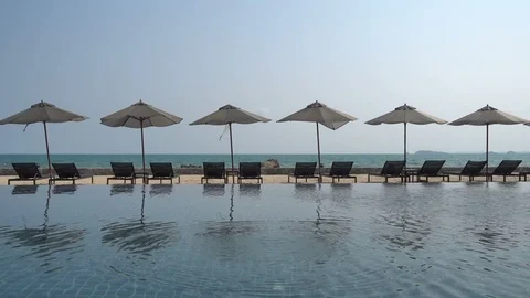 Empty beach lounges by a calm pool overlook the ocean on a tropical beach. Stock Footage 104786289