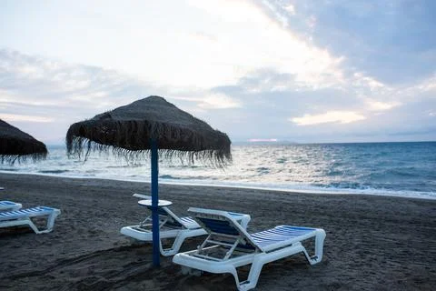 Empty beach with a straw umbrella and sun loungers at dusk against a calm sea Stock Photos