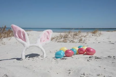 Empty beach on sunny day with Easter bunny ears and colorful plastic toy eggs Stock Photos