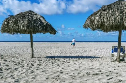 Empty beach, two beach umbrellas, a chaise longue, the figure of a man walkin Stock Photos
