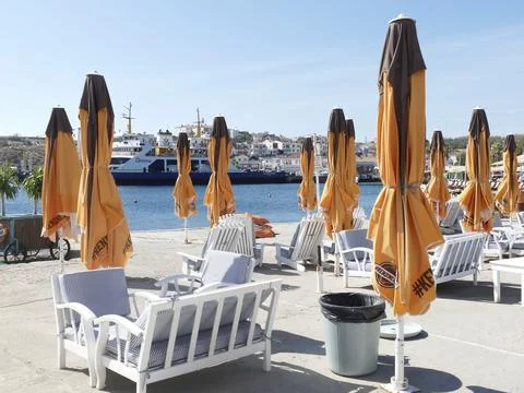 Empty beach with umbrellas and ferry approaching island harbor Stock Photos