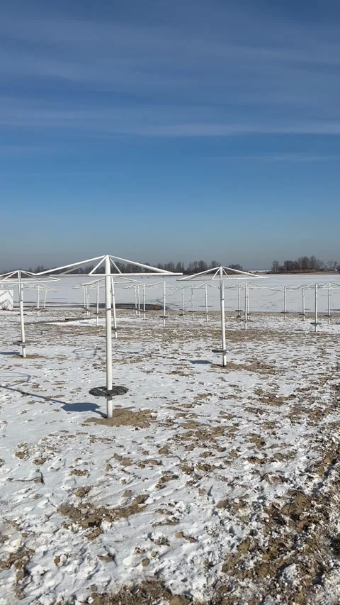 Empty beach umbrellas standing on a snow-covered beach on a bright, winter day Video stock 336260761