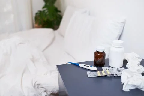 An empty bed with bedside table filled with treatments for flu - pills, tissues Stock Photos