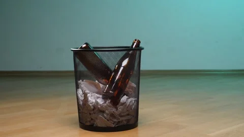 Empty beer bottles and crumpled paper filling a black wire mesh trash bin Stock Footage 342764116