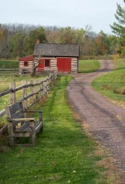 Empty bench along rustic rural lane by log cabin. Stock Photos