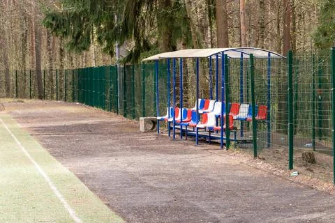 Empty bench and covered dugout overlooking playing field surrounded by forest Stock-Fotos