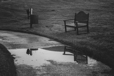 Empty bench and a lamppost are reflecting in a puddle on a path in a desert.. Stock Photos