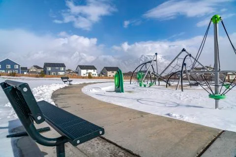 An empty bench facing a playground with snow covered ground in winter Stock Photos