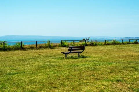 Empty bench on a hill on the ocean shore, green lush vegetation, a wooden Stock Photos