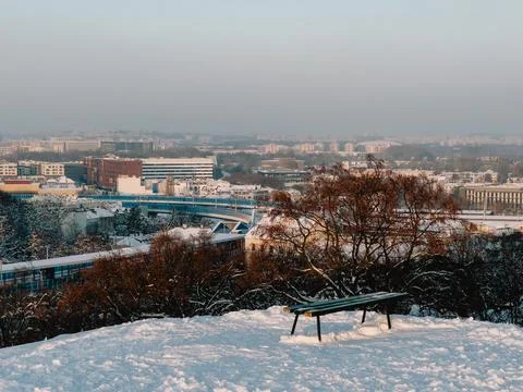 Empty bench sits on snow covered hill, overlooking cityscape of Krakow, Poland Stock Photos
