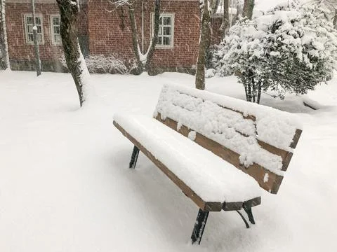 Empty bench under snow in winter at garden of a house while snowing Stock Photos