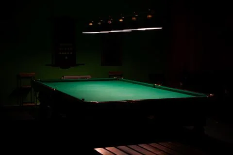 An empty billiard table, bathed in lamplight against a dark background. Stock Photos