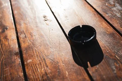 Empty black ashtray casting shadow on wooden table Stock Photos