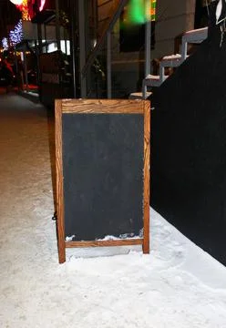Empty black board with a wooden frame and colorful lights, on the snow around Stock Photos