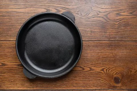 Empty black cast iron skillet on wooden table surface Stock Photos