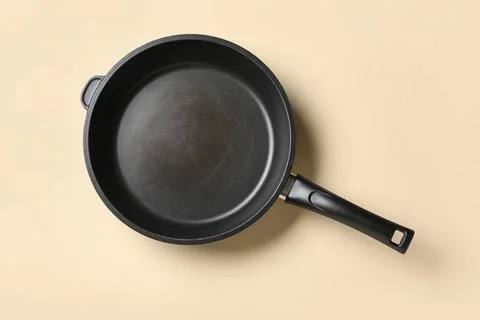 Empty black frying pan with non-stick coating and handle on a neutral beige b Stock Photos