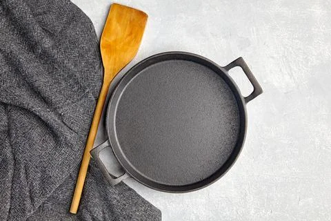 Empty black iron empty frying pan, wooden spatula and gray kitchen towel on a Stock Photos