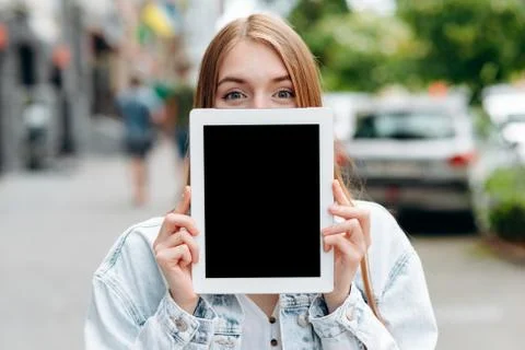 Empty black mockup ipad screen in female hands. Girl peeping from behind a sc Stock Photos