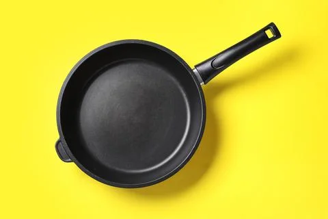 Empty black non-stick frying pan with handle on bright yellow background, top Stock Photos